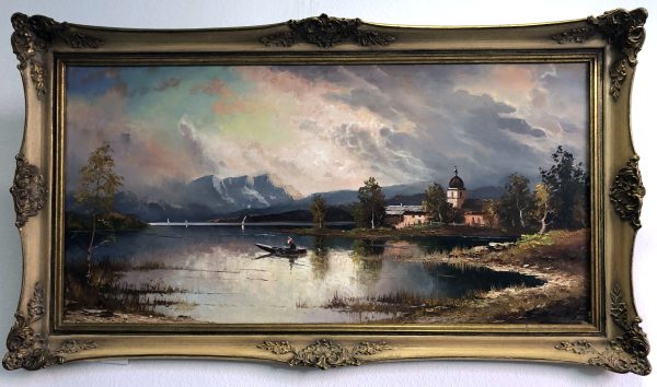 Gerahmtes Gemälde eines ruhigen Sees mit einem Ruderboot, fernen Bergen, Bäumen und einer Kirche am Ufer unter einem dramatischen, wolkenverhangenen Himmel. Der Rahmen ist verschnörkelt und goldfarben.