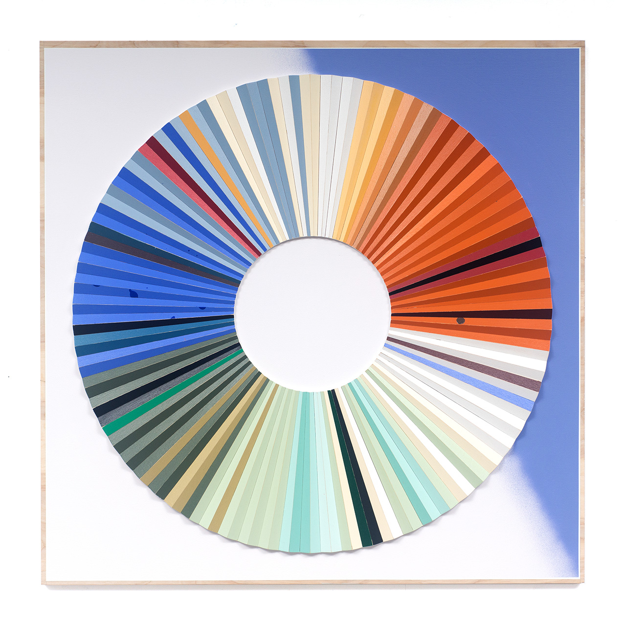 Ein quadratisches Kunstwerk zeigt ein großes kreisförmiges Muster aus bunten, länglichen Segmenten, die radial angeordnet sind. Die Segmente gehen von kühlen Blau- und Grüntönen auf der linken Seite zu warmen Orangen und Rottönen auf der rechten Seite über. Der Hintergrund ist weiß und blau.