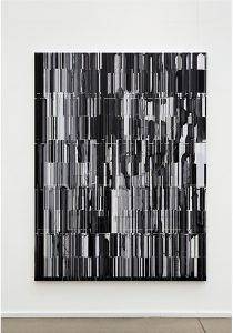 Ein großes abstraktes Gemälde mit vertikalen schwarzen, weißen und grauen Streifen unterschiedlicher Dicke und Länge, die auf einer weißen Wand angebracht sind. Das Design wirkt fragmentiert und glitchartig.