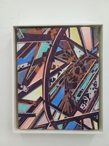 Abstraktes Gemälde mit sich kreuzenden geometrischen Formen und Linien in Blau-, Rosa-, Braun- und Gelbtönen, gerahmt in einer weißen Schattenbox und an einer weißen Wand montiert.