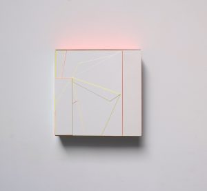 Ein weißes quadratisches Kunstwerk mit geometrischen Linien in Gelb und Orange, die in einem abstrakten Muster angeordnet sind, montiert an einer weißen Wand. Von der Oberseite des Werks geht ein sanftes rosa Leuchten aus.