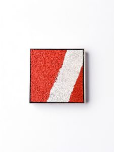 Ein rechteckiger, mit rotem, strukturiertem Material gefüllter Rahmen mit einem diagonalen weißen Streifen, der von links oben nach rechts unten verläuft, auf einem einfarbigen weißen Hintergrund.