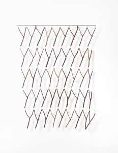 Ein minimalistischer Wandbehang aus natürlichen Zweigen, die mit Schnur in einem Rautenmuster zusammengebunden sind und an einer horizontalen Stange vor einem weißen Hintergrund hängen.