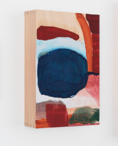 Abstrakte Malerei auf einem Holzblock mit markanten Formen in Rot, Blau, Rosa und Weiß, wobei auf der linken Seite die Holzmaserung sichtbar ist. Das Kunstwerk hängt an einer weißen Wand.